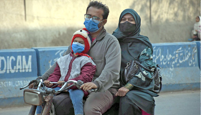 A family wearing facemasks moving on bike towards their way in Karachi on January 8, 2024. — Online