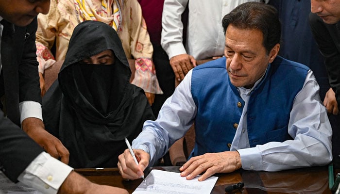 PTI founder Imran Khan (right) along with his wife Bushra Bibi (left) signs surety bonds for bail in various cases, at a registrar office in the High court, in Lahore on July 17, 2023. — AFP