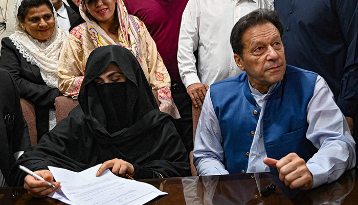 Former prime minister Imran Khan (right) along with his wife Bushra Bibi (left) looks on as he signs surety bonds for bail in various cases, at the Lahore High Court Registrar Office on July 17, 2023. — AFP