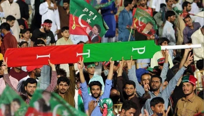 Supporters of former prime minister Imran Khan hold a giant cricket bat with the colours and initials of the party in Multan on July 20, 2018. — AFP