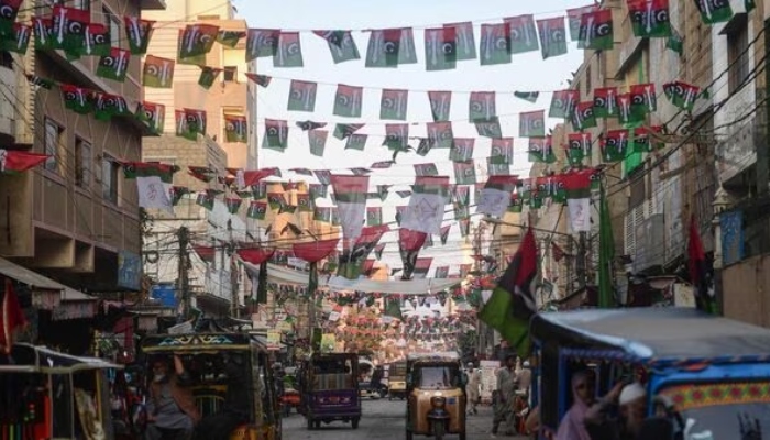 Commuters move past the flags of political parties hung over a street in Karachi on January 17, 2024. —AFP