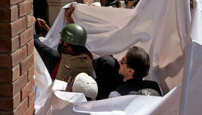 Former prime minister Imran Khan and his wife Bushra Bibi are covered with a white sheet as they arrive to appear at the high court in Lahore on May 15, 2023. —Reuters