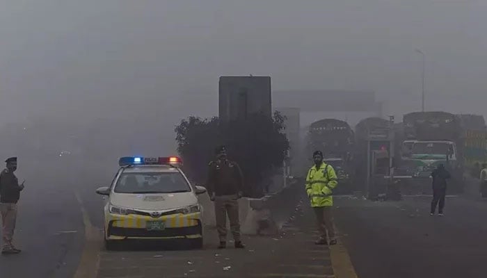 Traffic policemen stand along a motorway in Lahore amid dense fog. — AFP/File