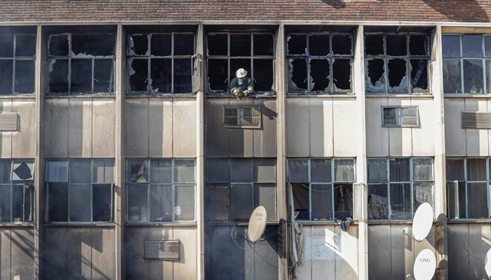 A firefighter looks out of broken windows at the scene of a fire in a building in Johannesburg on August 31, 2023. — AFP