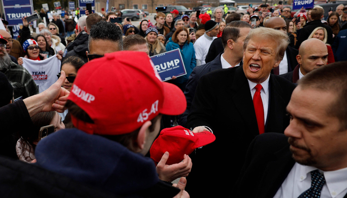 Former US President Donald Trump autographs hats while visiting with supporters outside the polling site at Londonderry High School on January 23, 2024 in Londonderry, New Hampshire. — AFP