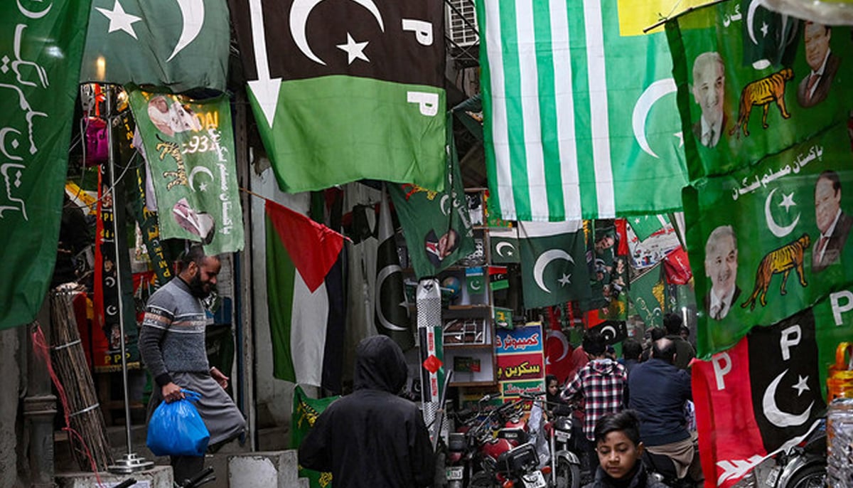 People walk past flags of Pakistans political parties displayed for sale at a market in Lahore on January 13, 2024. — AFP
