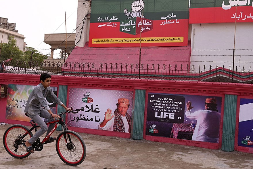 A boy rides past wall posters with images of PTI founder Imran Khan in Hyderabad on January 30, 2024. — AFP