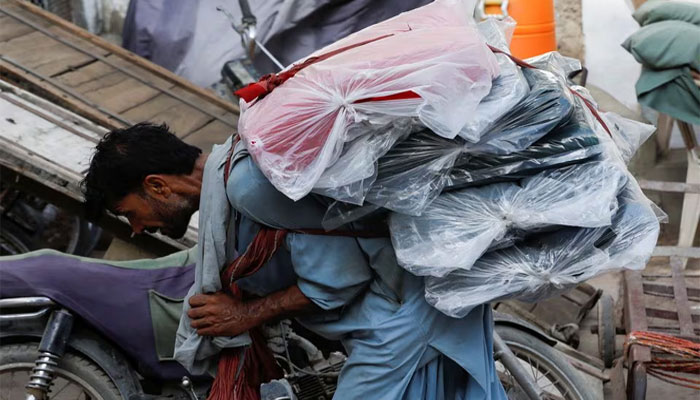A labourer bends over as he carries packs of textile fabric on his back to deliver to a nearby shop in a market in Karachi, Pakistan June 24, 2022. — Reuters