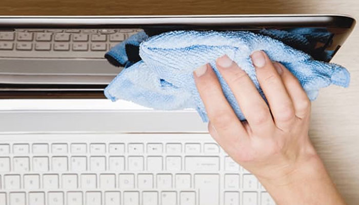 An individual cleaning a laptop screen with a microfiber cloth. — HP