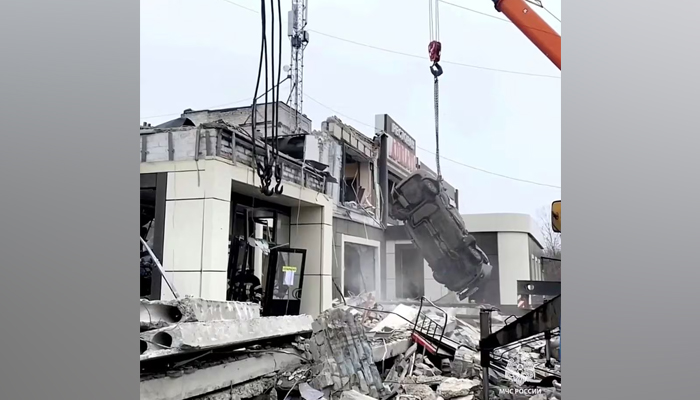 ایک کرین تباہ شدہ گاڑی کو ملبے کے نیچے سے اٹھا رہی ہے کیونکہ 3 فروری 2024 کو ریلیز ہونے والی ویڈیو سے لی گئی اس اسکرین گریب میں، یوکرین کے لوہانسک میں، پس منظر میں ایک تباہ شدہ عمارت نظر آ رہی ہے۔ - رائٹرز