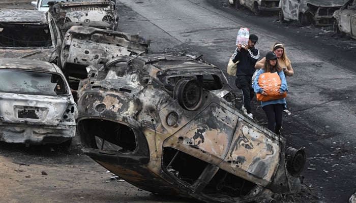 People walk past burned vehicles after a forest fire in Quilpue, Viña del Mar, Chile, on February 4, 2024. — AFP