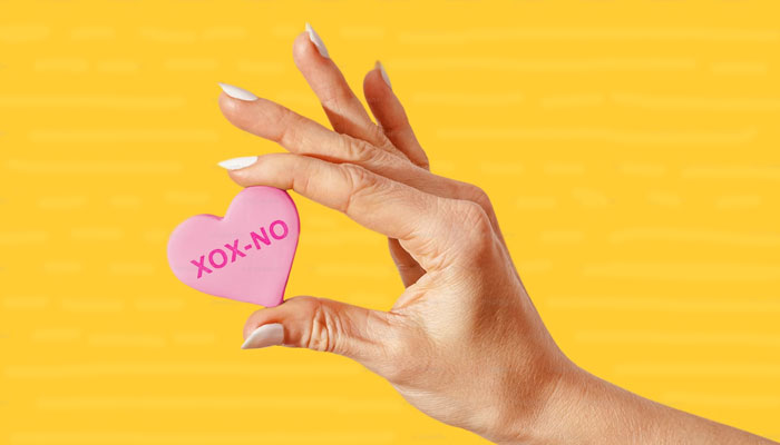 A woman holds a candy heart with the XOX-NO printed on it. — Unsplash