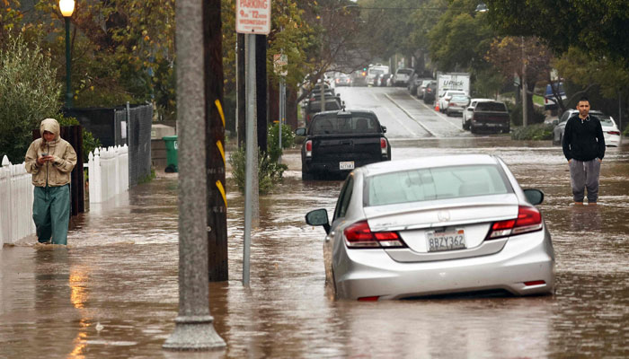 People gather along a flooded street as a powerful long-duration atmospheric river storm, the second in less than a week, impacts California on February 4, 2024, in Santa Barbara, California. — AFP