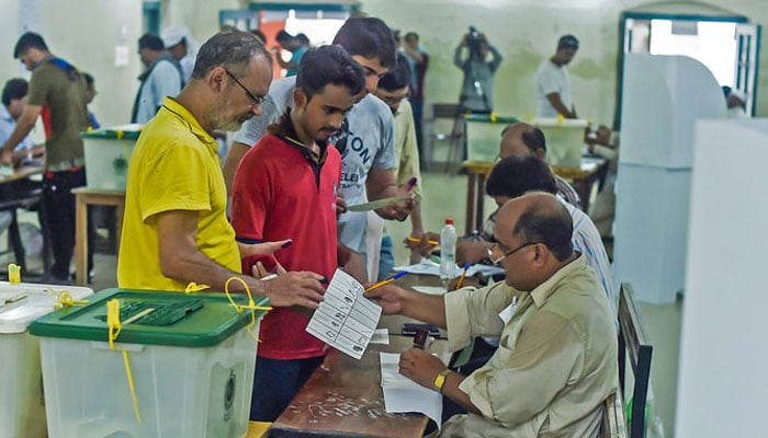 Pakistani men line up as election officials check their ballot papers during voting in Pakistans general election at a polling station in Lahore on July 25, 2018. — AFP