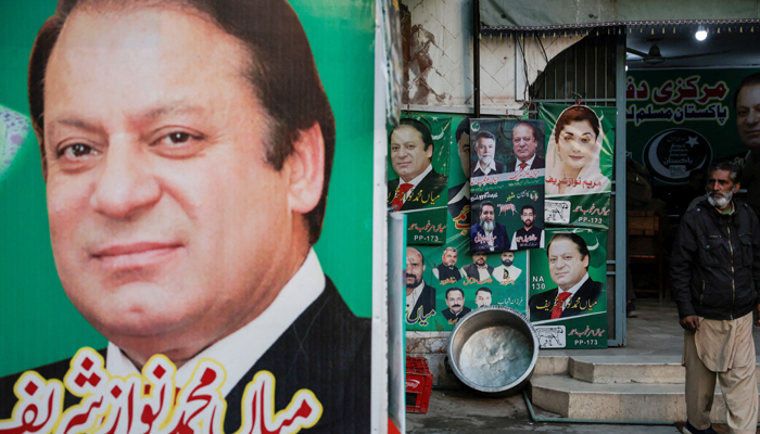 A man stands near the banner and campaign posters of Pakistans former prime minister Nawaz Sharif ahead of the general elections, in Lahore, February 5, 2024. — Reuters