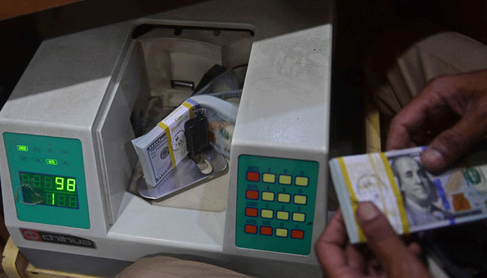 A currency exchange dealer counting $100 bills in a machine in this undated picture. — AFP/File
