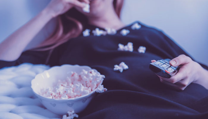 A woman eating popcorn while watching TV. — Unsplash