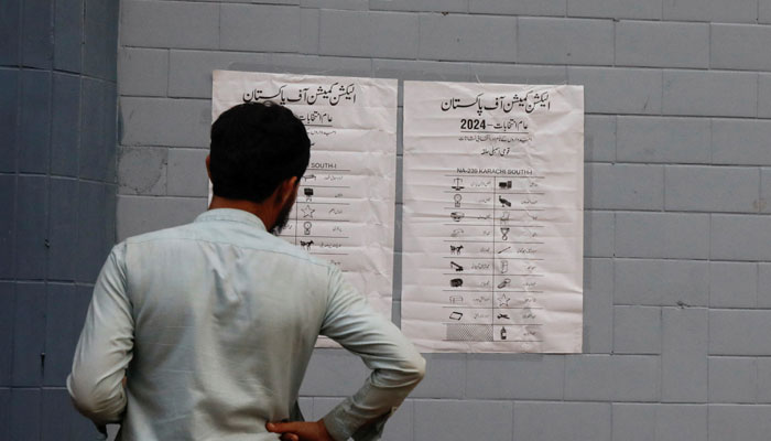 A man looks at the poster with the names of contesting candidates and their electoral signs, outside a polling office, set up for general election in Karachi, Pakistan February 7, 2024. — Reuters