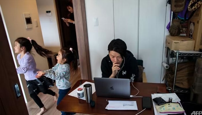 Yuki Sato, an employee in a startup company, works from home during the COVID-19 outbreak in Tokyo, as his daughters play and his wife Hitomi uses a mobile phone. —AFP/file