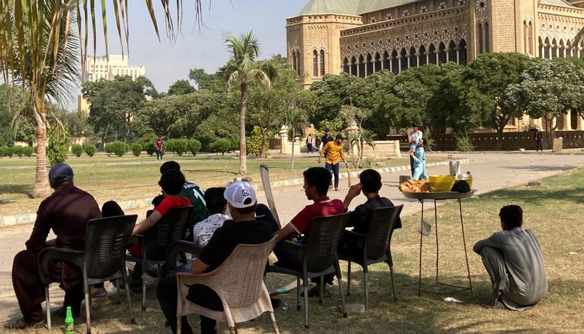 A group of young men sit watch a cricket match being played in the Frere Hall gardens. — Photo by author