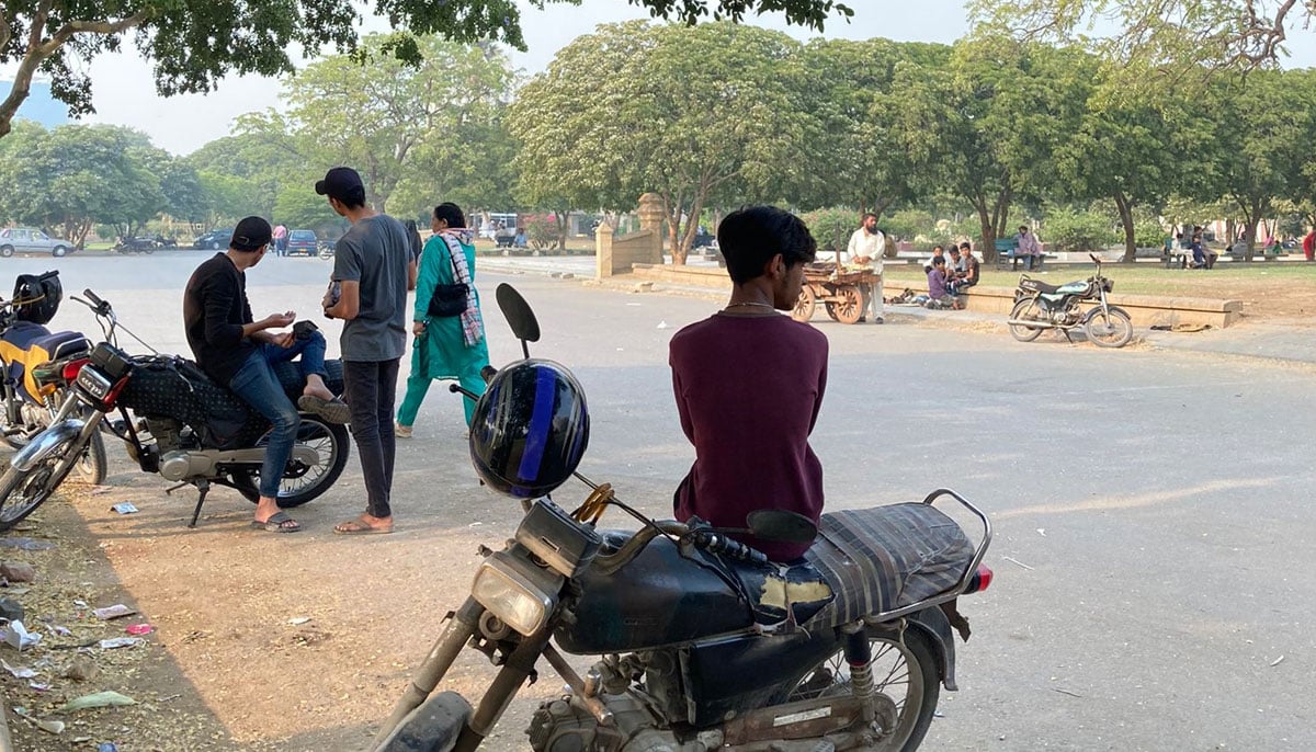 Young men seen seated on their motorcycles as a woman walks by at the Frere Hall. — Photo by author