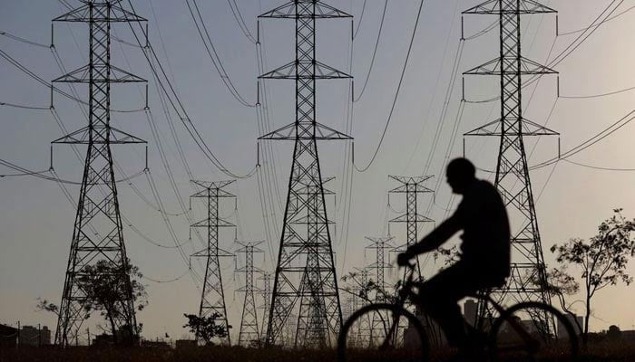 A man rides a bicycle near power lines connecting pylons of high-tension electricity. — Reuters/File