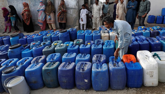 Residents gather as a worker fills containers at a free water distribution point in Orangi Town on the outskirts of Karachi, on March 19, 2021. — Reuters
