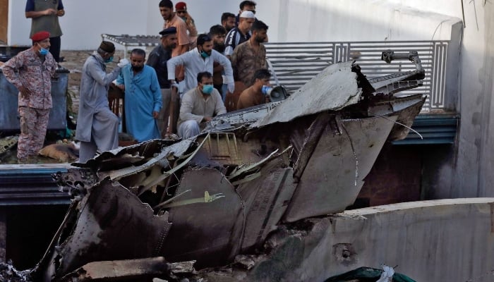 People stand next to the debris of a plane after crashed in a residential area near an airport in Karachi on May 22, 2020. —Reuters