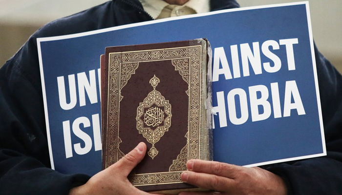A person holds the Holy Quran and a protest sign mentioning unite against Islamophobia during a demonstration in this undated image. — Reuters