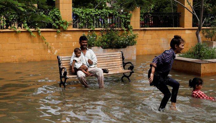 A man with a baby sits on a bench while children play amid flooded street during the monsoon season in Karachi, July 11, 2022. — Reuters