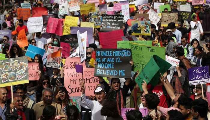 Women and men carry signs as they take part in Aurat March in Lahore on March 8, 2020. — Reuters