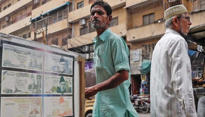 People walk past a sidewalk money exchange showcase, which is decorated with pictures of currency notes, in Karachi on September 12, 2023. —Reuters