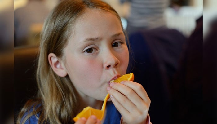 A young girl eating an orange. — Pixabay