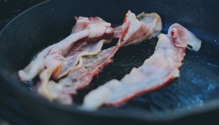 This image shows bacon being cooked on a skillet. — Unsplash