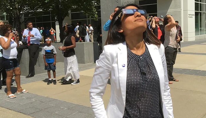 A woman and people surrounding her look toward the solar eclipse with specific glasses to safely view the Sun during the partial eclipse. — Nasa/Mamta Patel Nagaraja