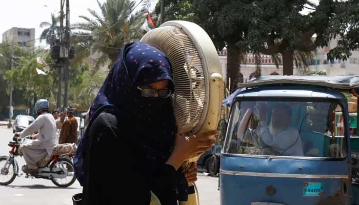 A woman carries a pedestal fan as she walks towards a repair shop during hot and humid weather in Karachi. — Reuters/File
