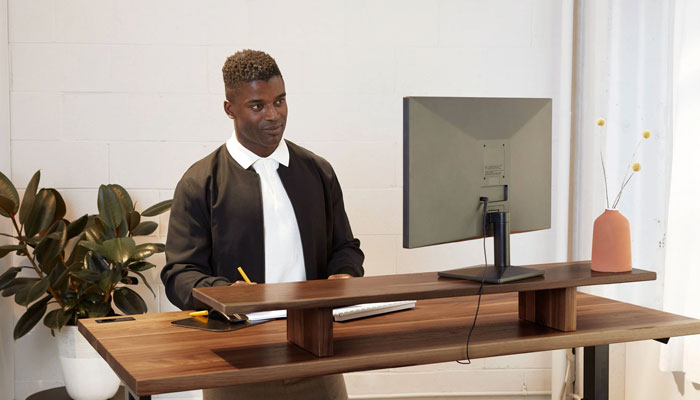 This image shows a man working on computer in front of a sit-stand desk. — Ergonofis