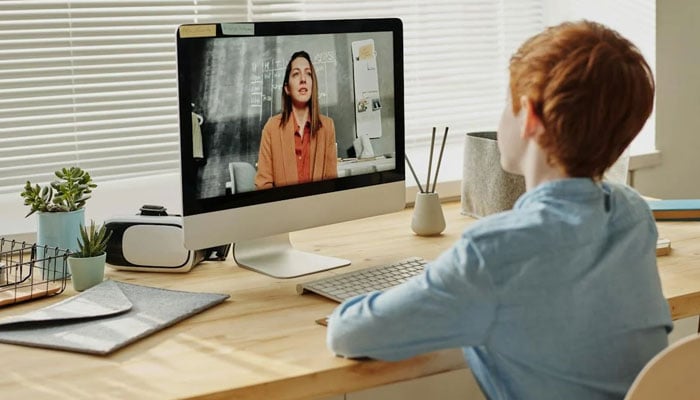 This image shows a child watching video on a compuer while sitting. — Pexels