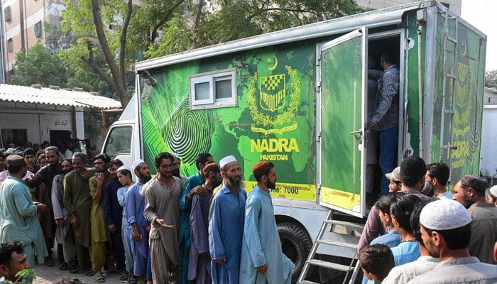Afghan refugees wait outside a National Database and Registration Authority (NADRA) van for their data verification, at a police station in Karachi on November 8, 2023. — AFP