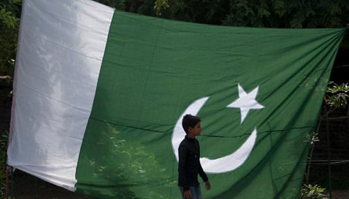 A boy walks past a Pakistani flag displayed for salealong a road in Rawalpindi. — Reuters/File