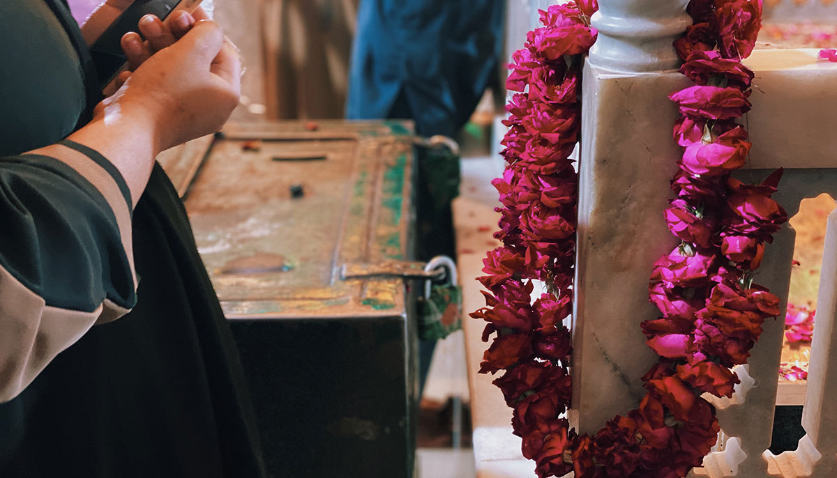 A woman praying after she puts flowers on the marble railing near the shrine in the courtyard of the Bibi Pak Daman. — Photo by author