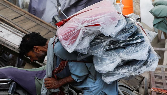 A labourer bends over as he carries packs of textile fabric on his back to deliver to a nearby shop in a market in Karachi. — Reuters/File