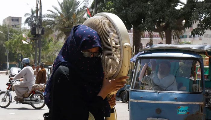 A woman carries a pedestal fan for repair during a hot and humid weather in Karachi. — Reuters/File