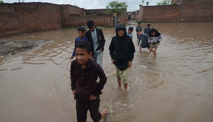 Children crossing flooded are after rain in Peshawar on April 15, 2024. — INP