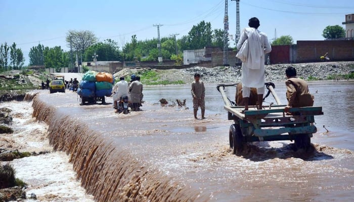 Vehicles and horse carts passing through flood water at Bara Bazar area on Khuwani bridge after heavy rain in Peshawar on April 17, 2024. —APP