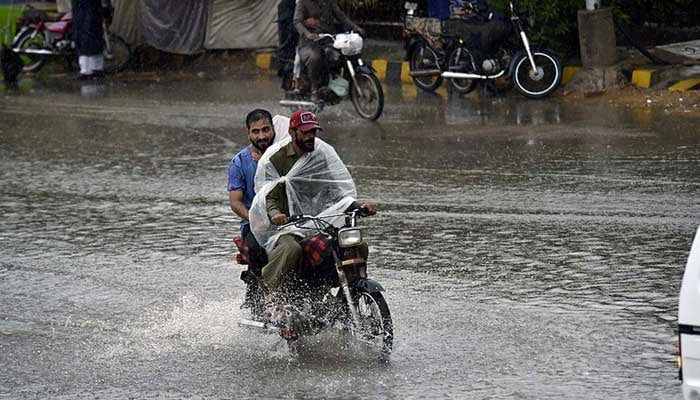 Motorcyclists are passing through a flooded road in Karachi amid heavy rain. — APP/File