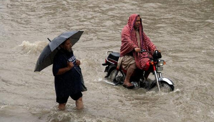A man holds an umbrella as he walks through floodwaters alongside another man riding a motorcycle during heavy rain in Lahore. — Reuters/File