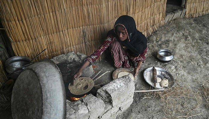 Najma Ali, a monsoon bride who was married underage, prepares flatbread outside her hut at Khan Muhammad Mallah village in Dadu district on August 3, 2024. – AFP