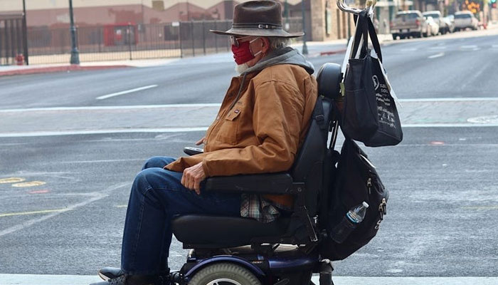 This undated photo shows an elderly disabled man in wheelchair travelling alongside the road. — Unsplash/File