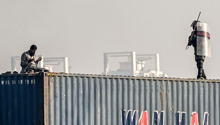 A supporter of the PTI on top of a shipping container as a law enforcer chases him during a protest demanding the release of former prime minister Imran Khan, at the Red Zone area in Islamabad on November 26, 2024. —  AFP
